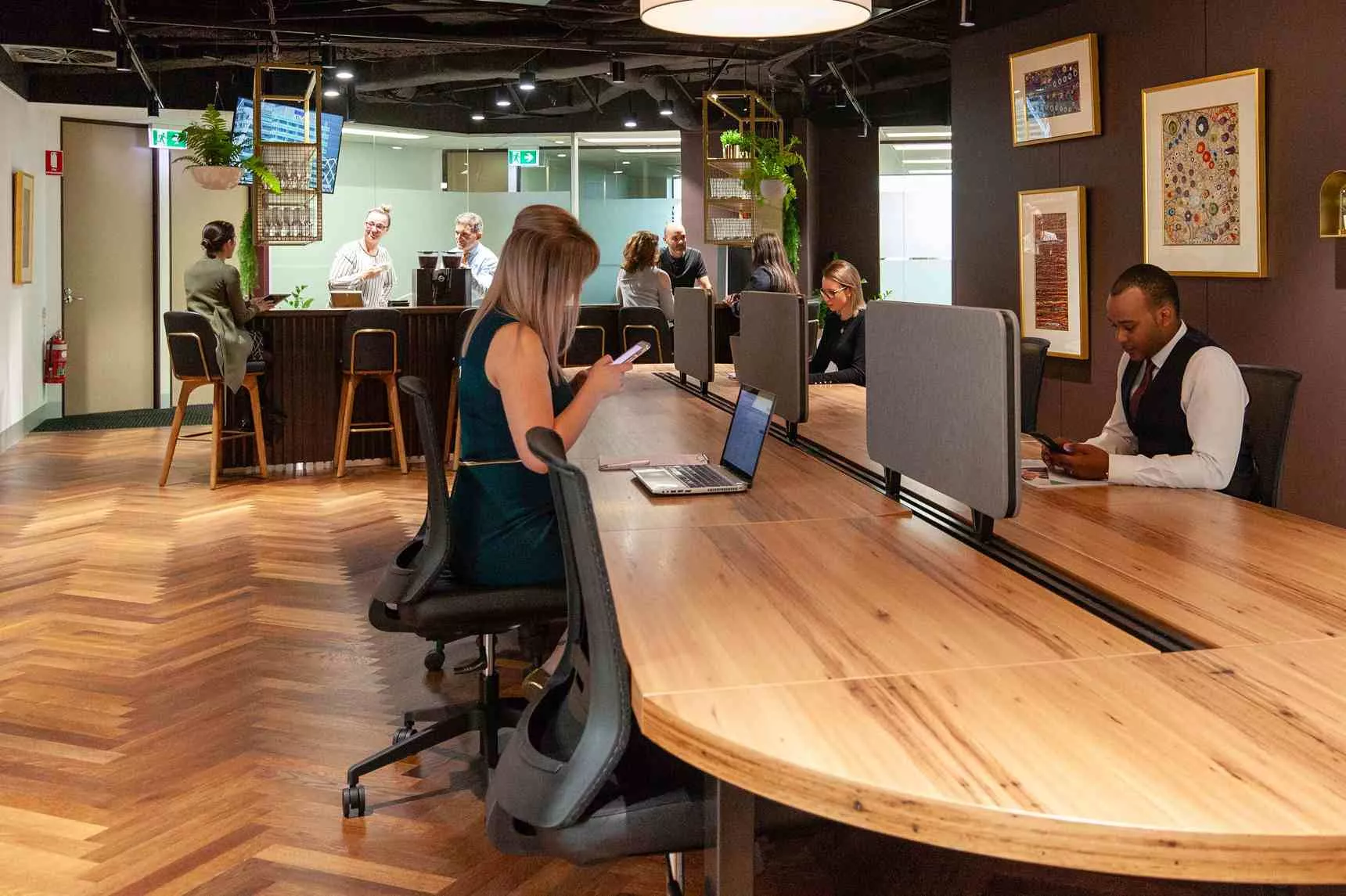 Clients working in a modern coworking shared space on a long table surrounding fully fitted kitchen in Servcorp 91 King William Street, Adelaide